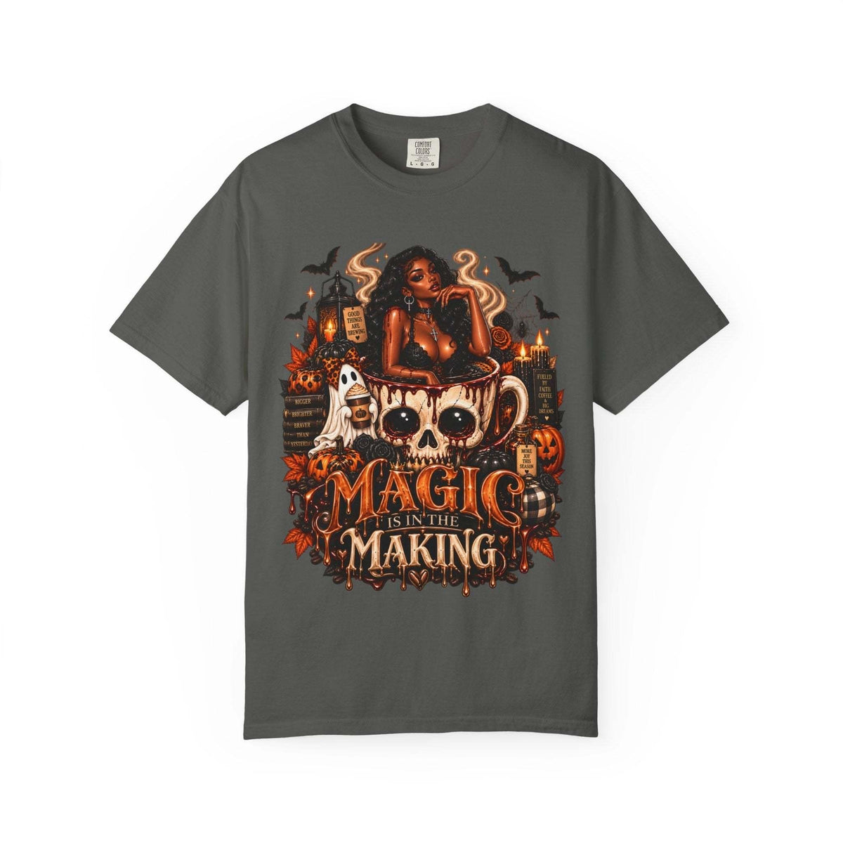 Unisex Garment-Dyed T-shirt in dark gray with a Halloween-themed graphic featuring a stylish woman, skull coffee mug, pumpkins, ghosts, bats, and candles with the text Magic Is in the Making